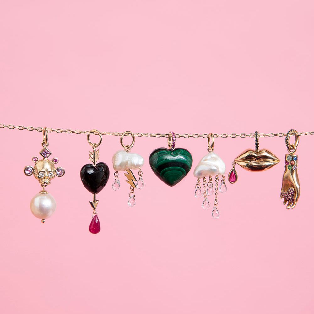 7 Rachel Quinn Jewelry Charms hanging horizontally across a chain on a pink background.
