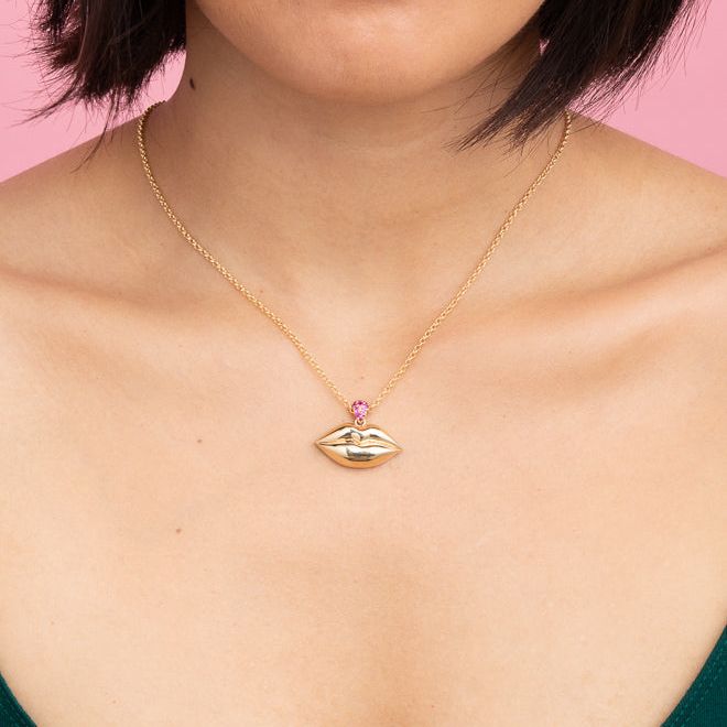 Large plump lips necklace in 14k yellow gold on gold chain with magenta sapphire bail shown on female neck.