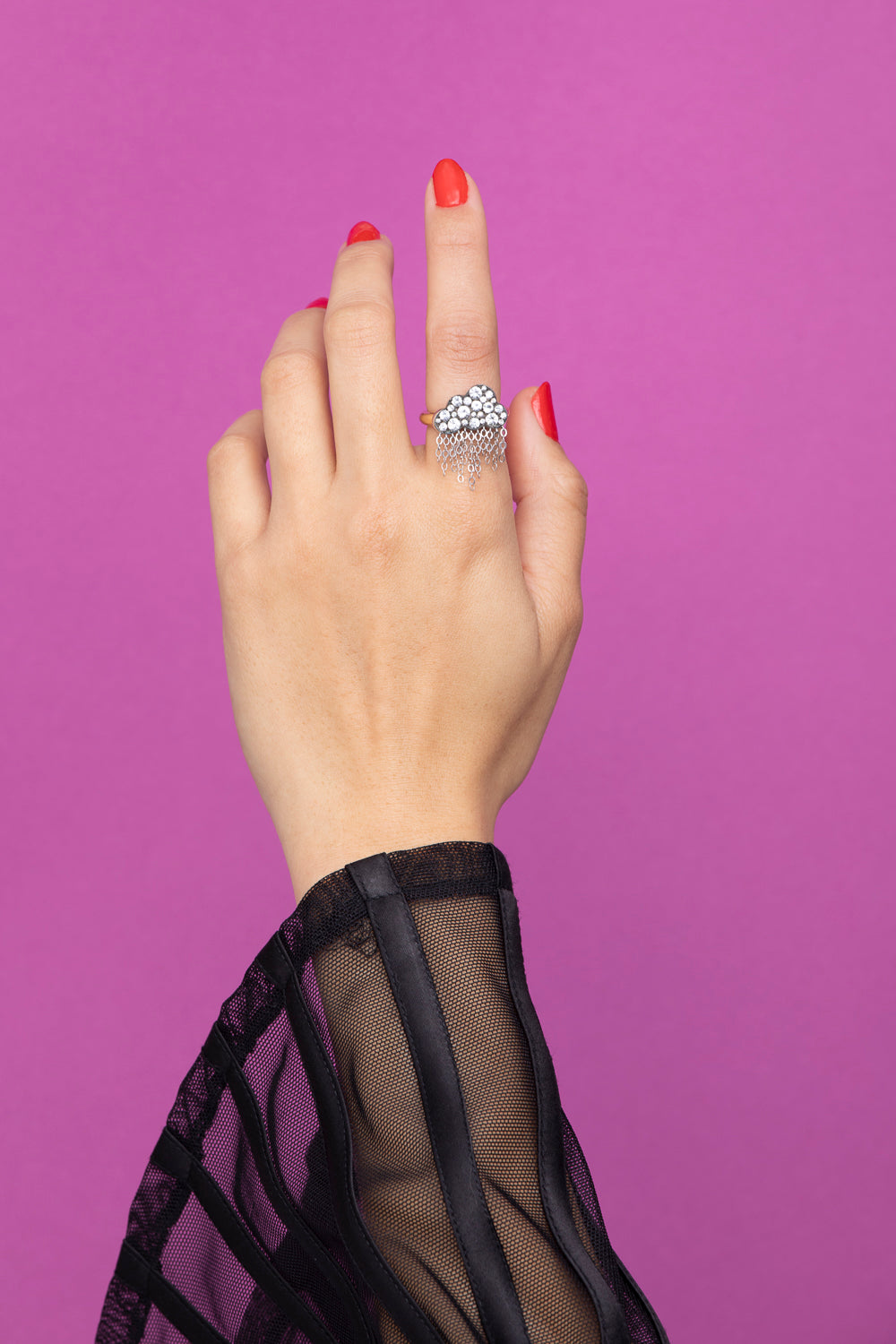 Rachel Quinn Jewelry black cloud shaped ring with pave white sapphires on cloud and dangling chains on yellow gold band on female model hand with purple background.