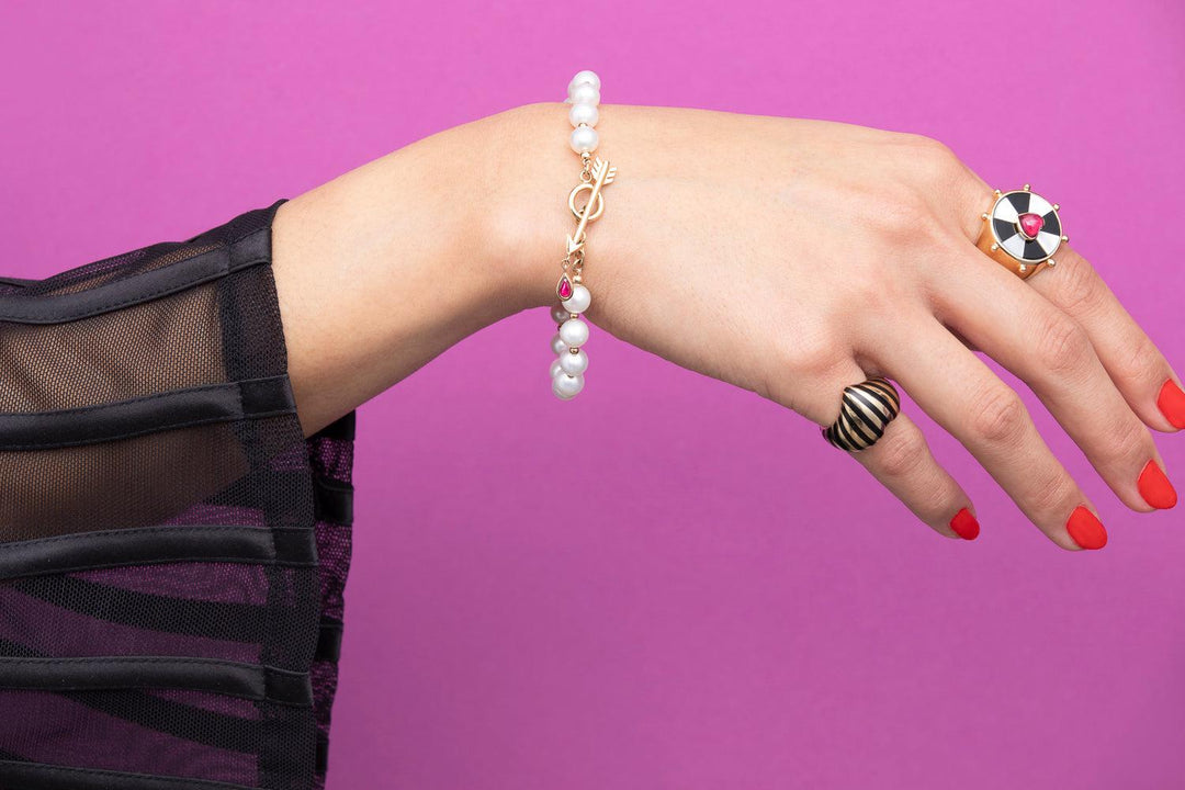 Model hand on pink background wearing a rachel quinn pearl bracelet and heart striped ring and bullseye ring