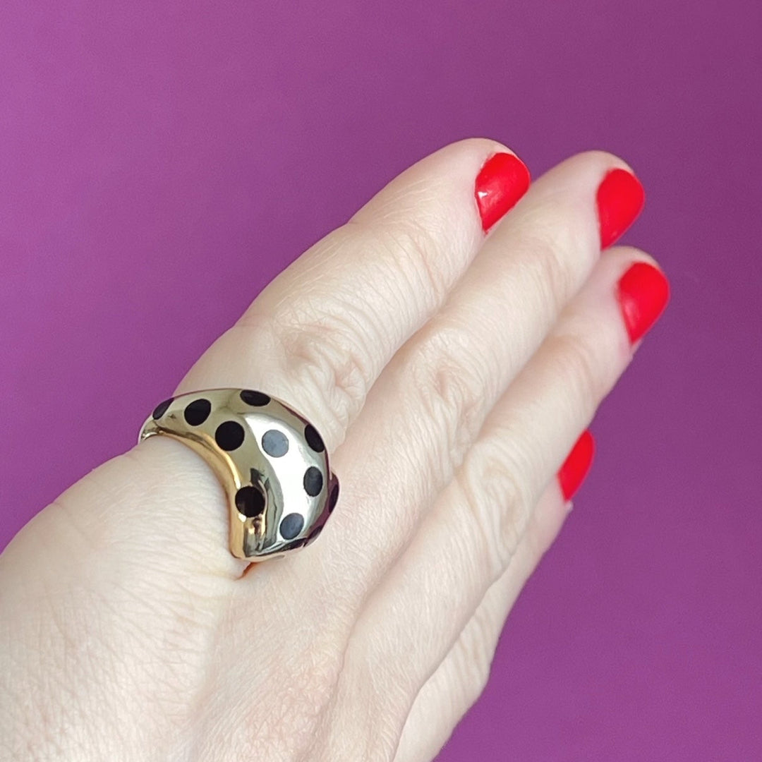 angled view of gold chubby heart ring with black polka dots on a pinky finger to show how the ring wears