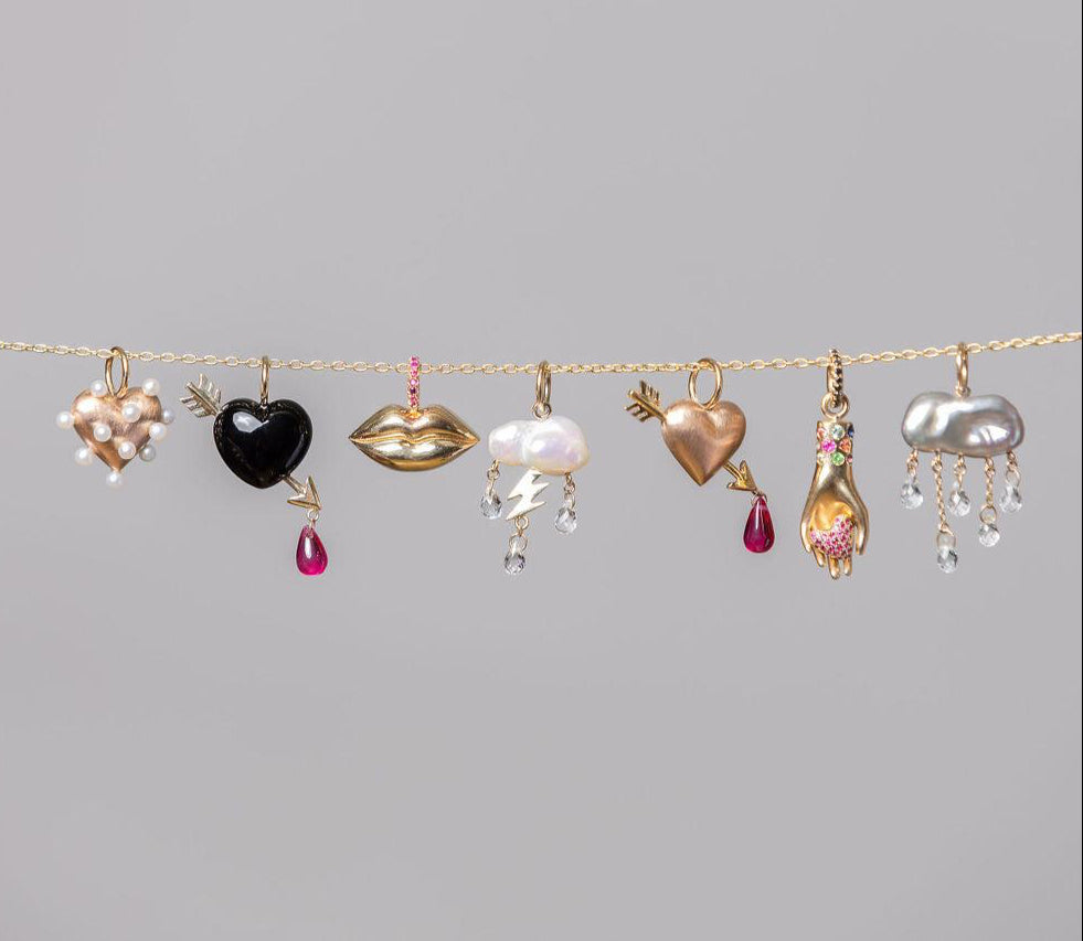 multiple different rachel quinn jewelry charms dangling from a gold chain horizontal with grey background