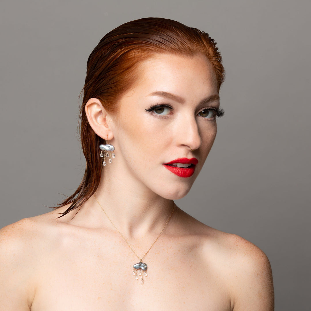 another woman modeling keshi pearl elongated puffy cloud shape charm on yellow gold necklace chain with 5 small tear drop white topaz raining down underneath and monsoon earring