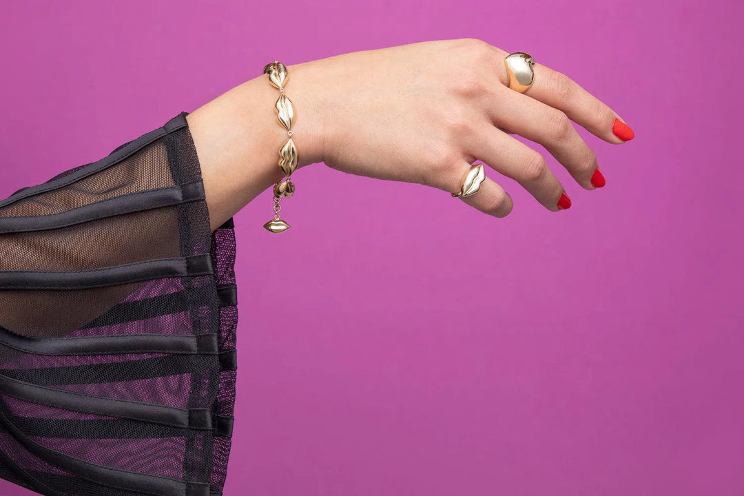 Rachel Quinn Jewelry 14k yellow gold connecting lips bracelet on model hand with purple background.