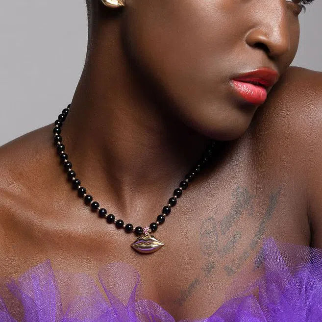 black model wearing gold lip earrings and black and gold lip necklace and purple dress