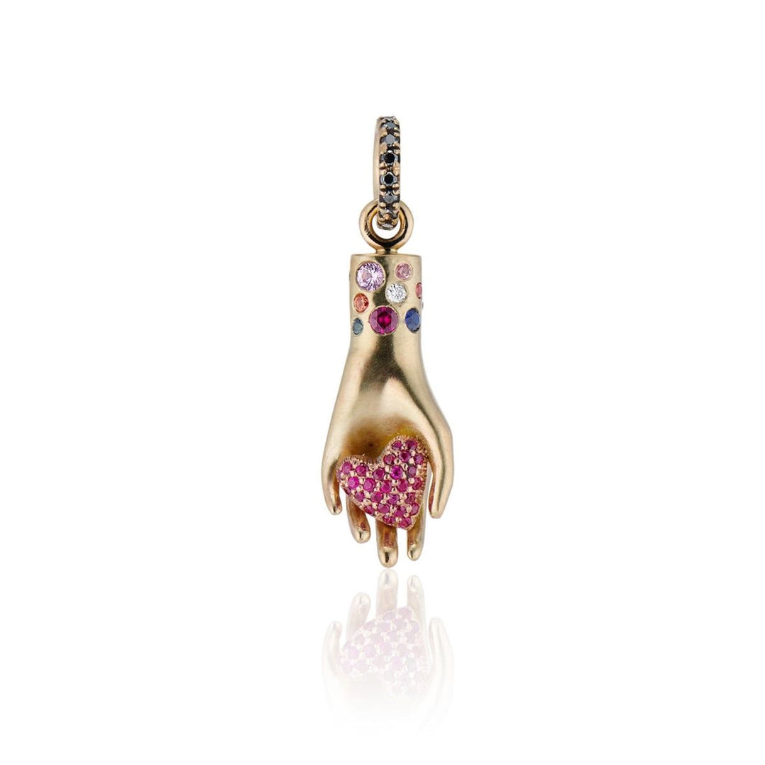gold hand with ruby puffy heart in palm and multi-colored sapphires around wrist with a black diamond bail charm on a white background