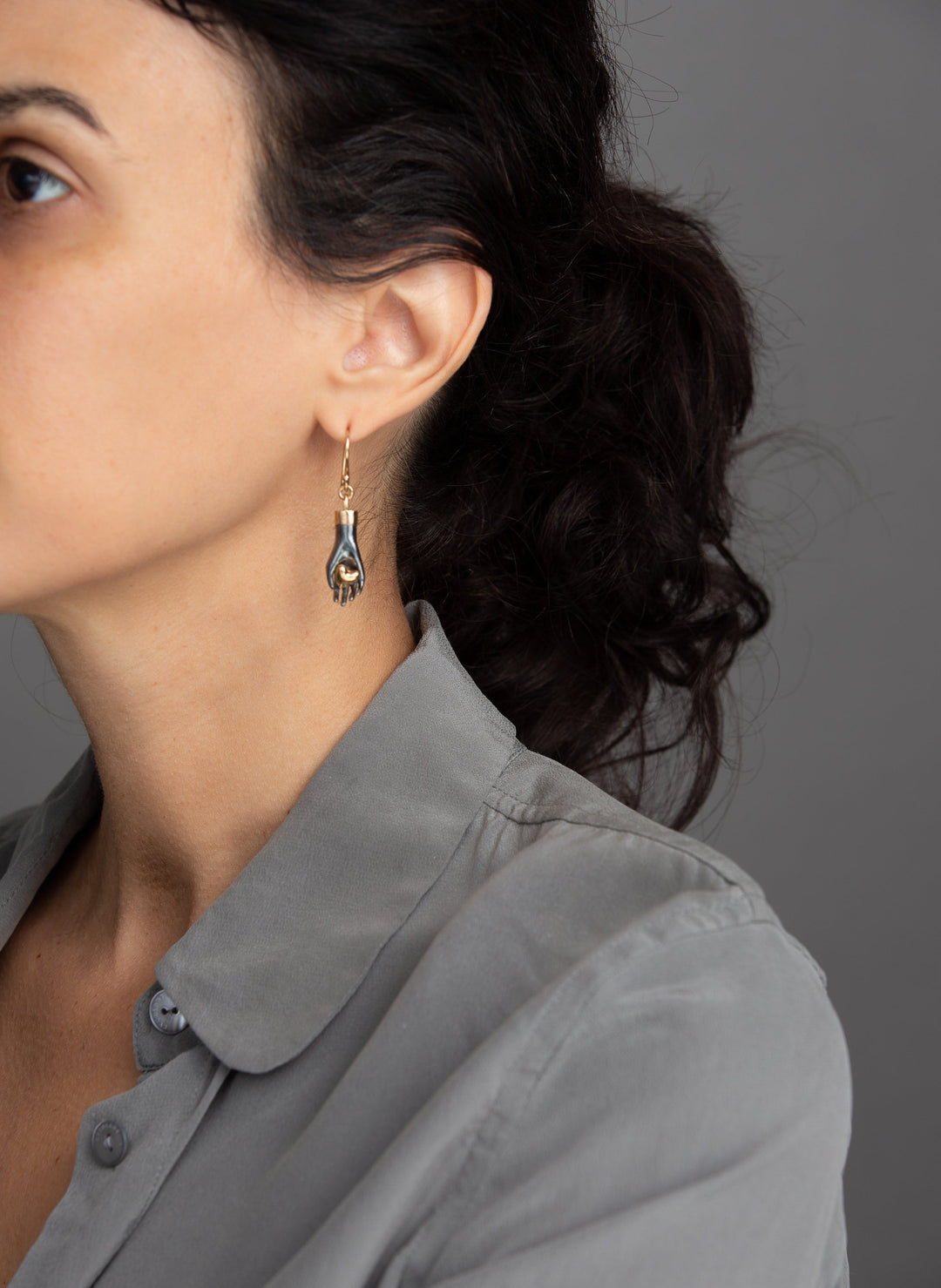 woman in grey modeling Sterling silver hand earring gently hold 14K solid rose gold heart. Wrist cuff and ear wire is made of yellow gold