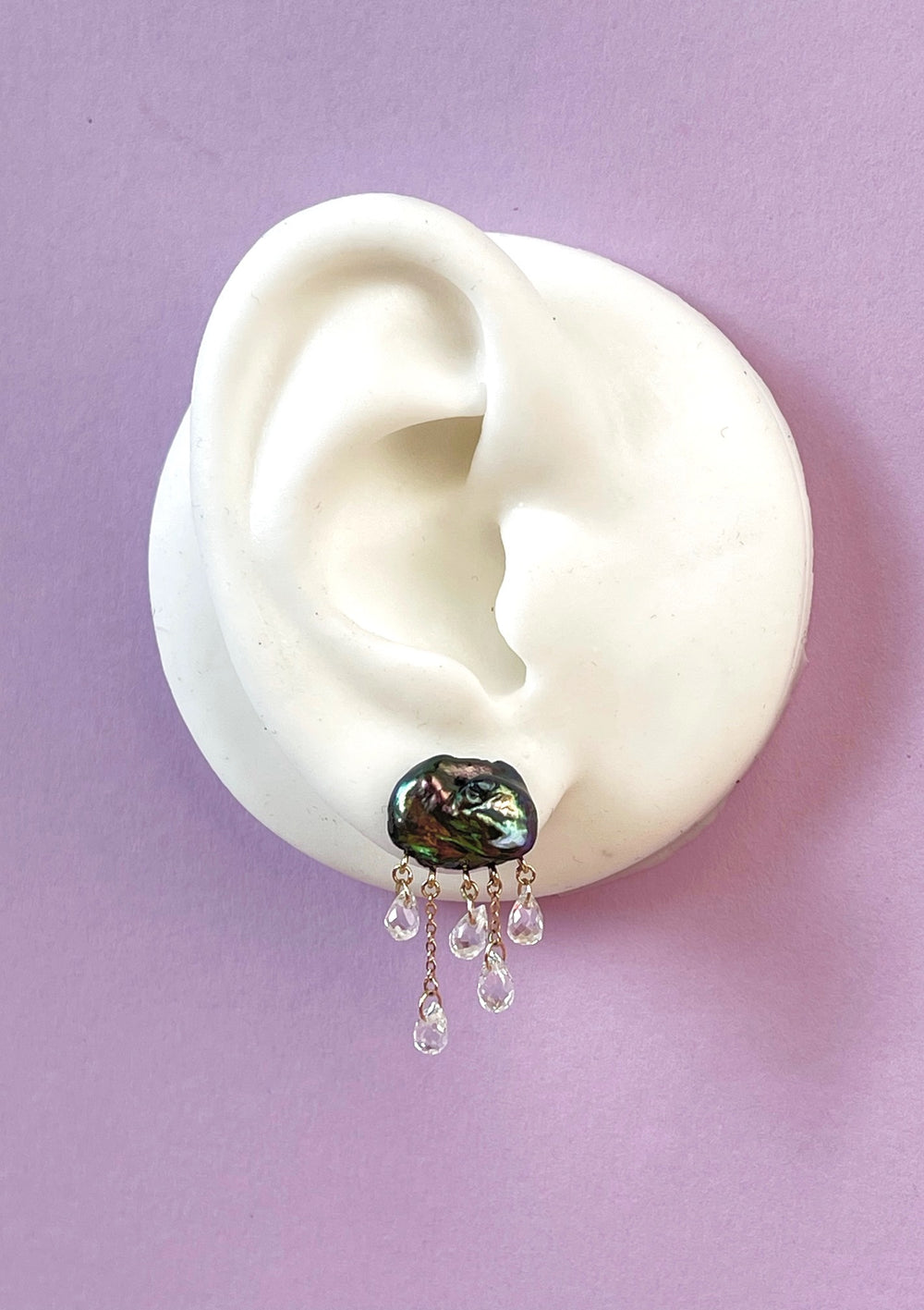 white ear shape one purple background with dark cloud-shaped pearl earring with 5 raindrops dangling below
