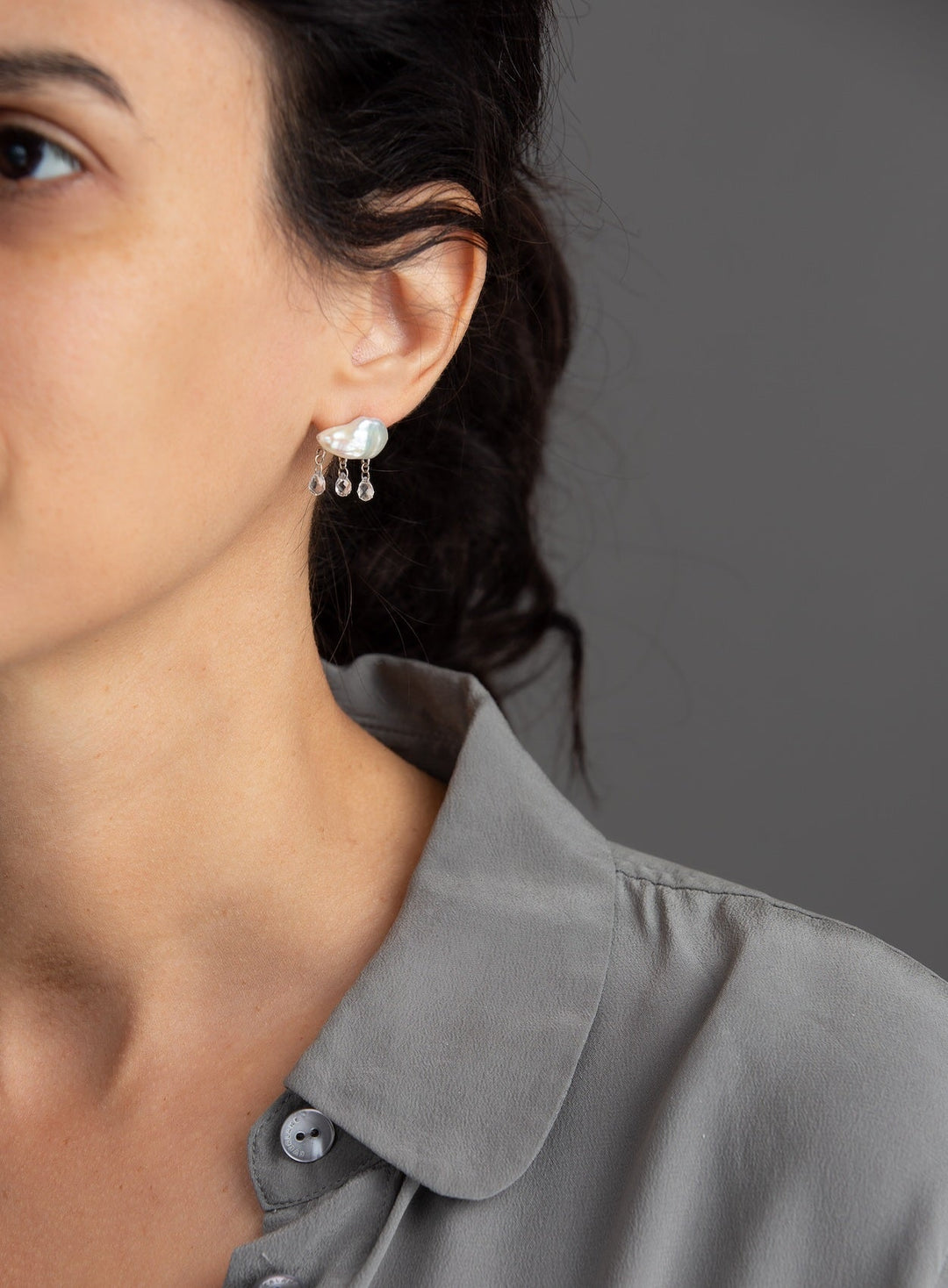 woman in grey modeling white keshi pearl earring in cloud-like form with three white topaz dangling from the bottom with yellow gold components