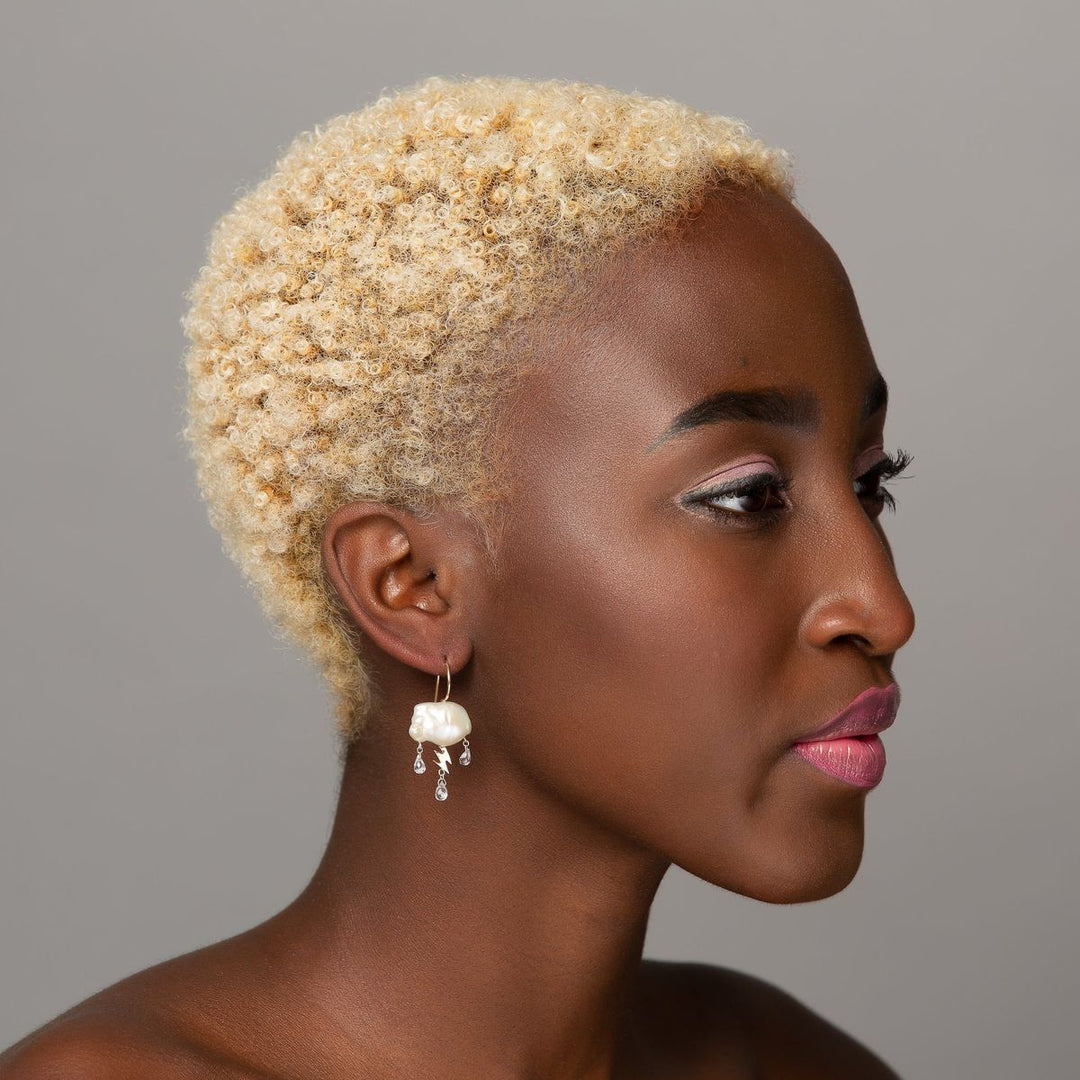 woman modeling a single white stormy keshi cloud like pearl earring with 14K yellow gold lightning bolt as a trio of white topaz rain down with gold ear wire