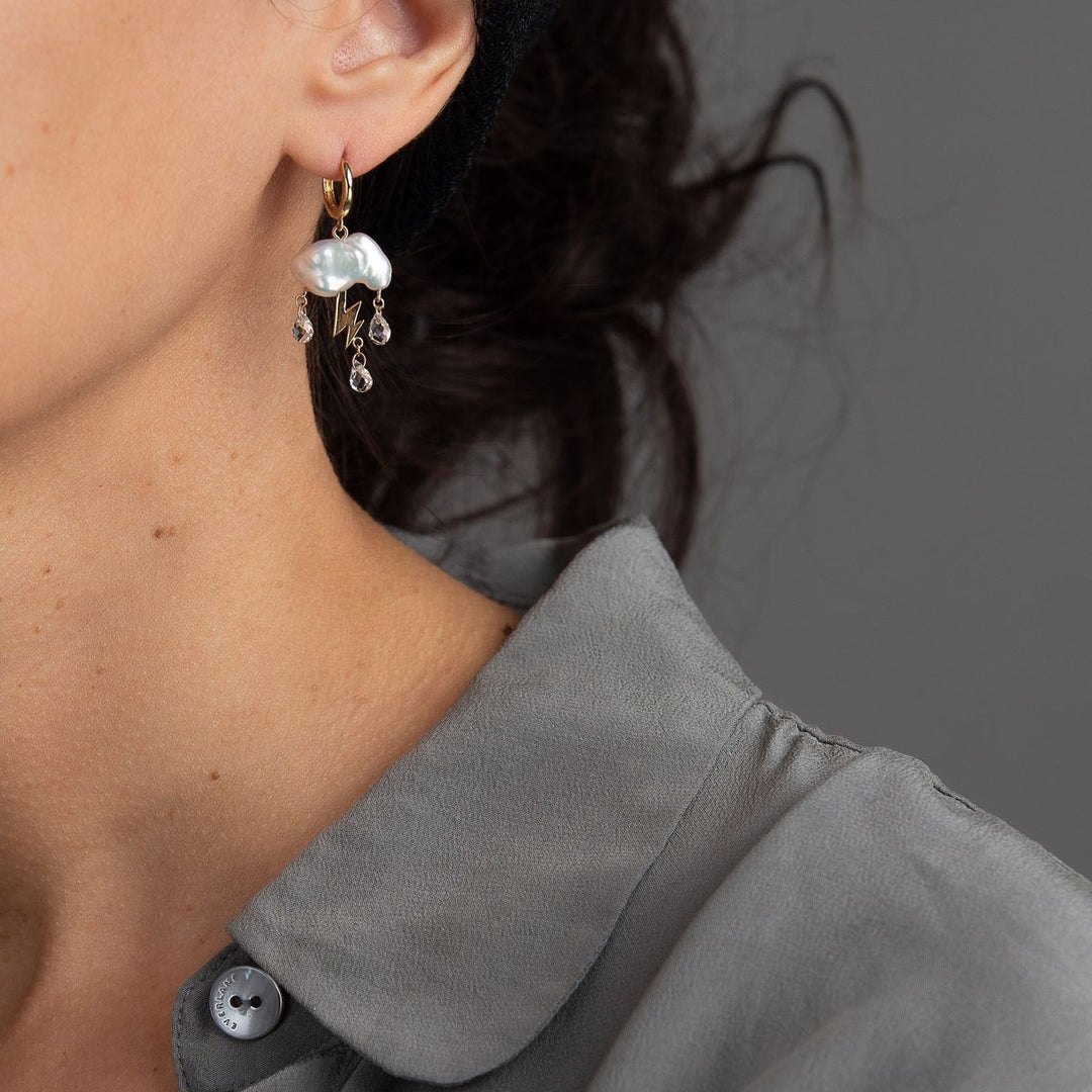 woman in grey modeling a single white stormy keshi cloud like pearl earring with 14K yellow gold lightning bolt as a trio of white topaz rain down with gold huggie hoop