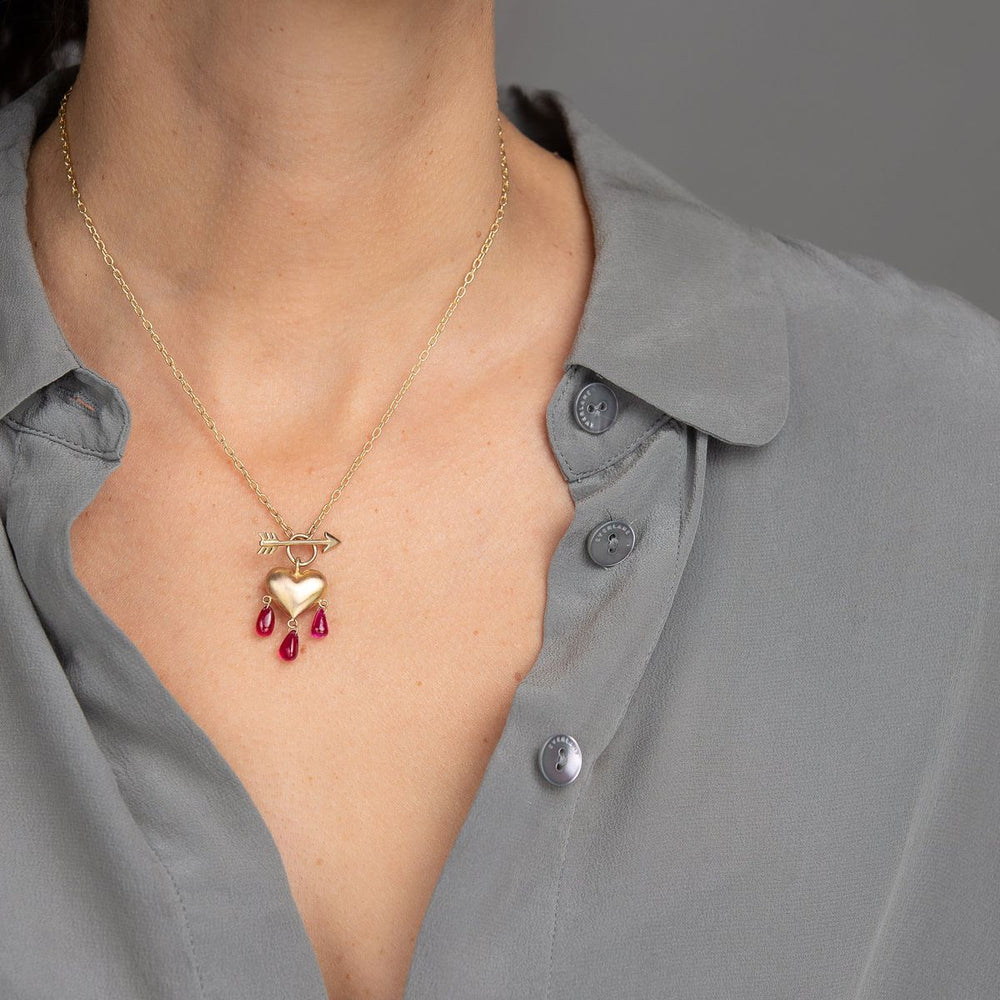 Woman in grey blouse wearing yellow gold puffed heart necklace with pink ruby droplets