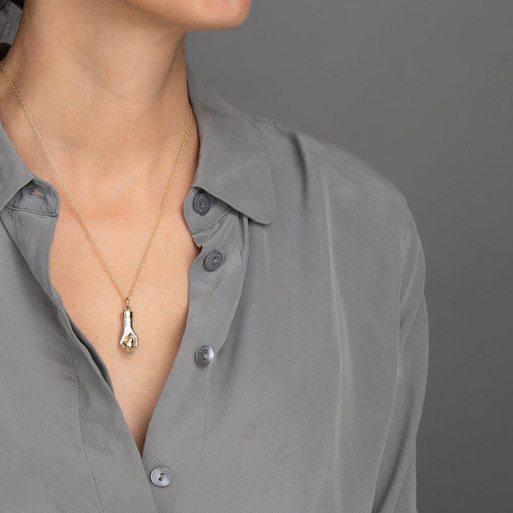 woman in grey models hand charm made of solid sterling silver gently holds a 14K rose gold heart with yellow gold wrist cuff and bail on yellow gold delicate chain necklace
