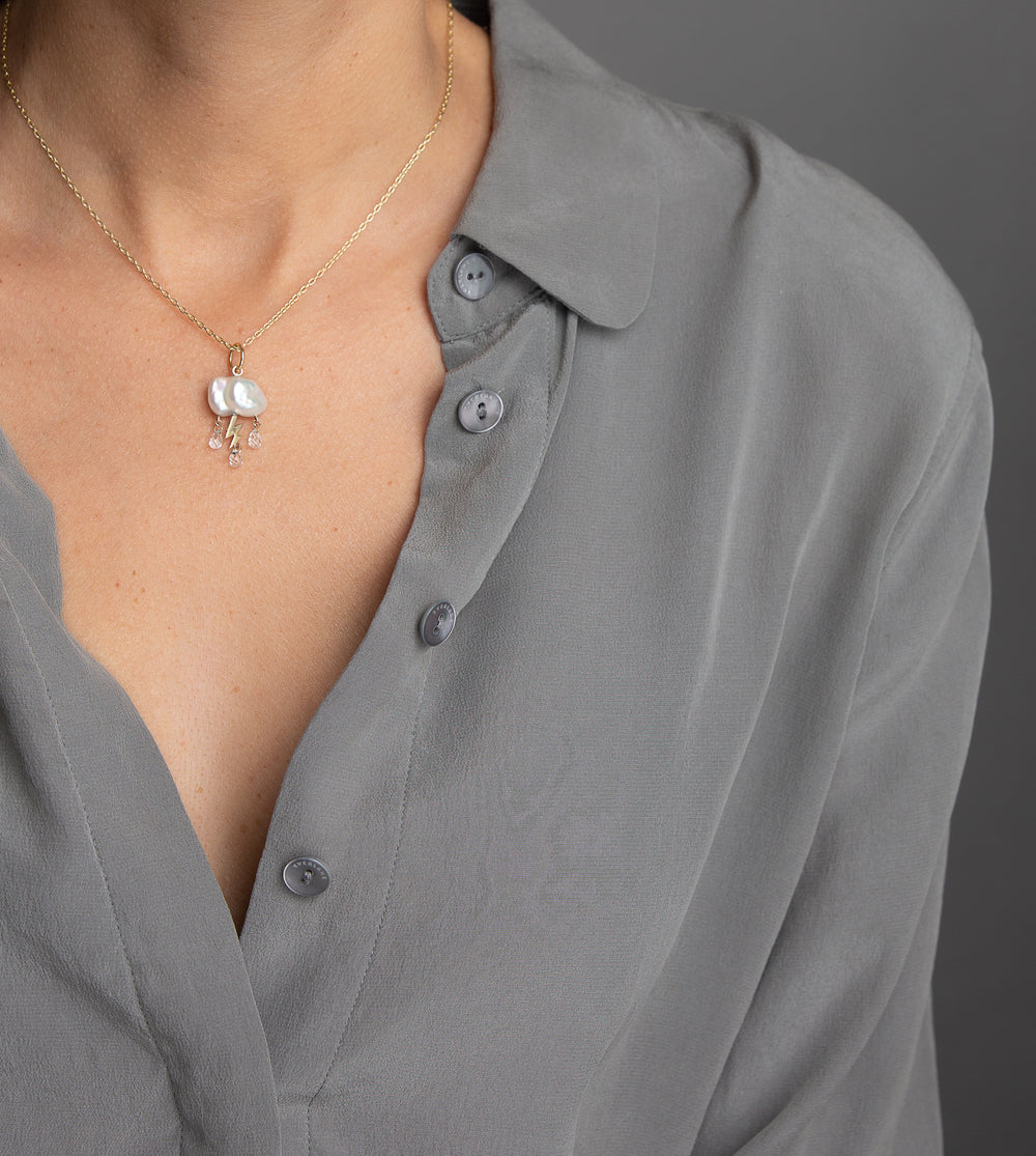 woman in grey modeling small keshi cloud like pearl charm with 3 white topaz rain drops from underneath and yellow gold lightening bolt of the center three on gold chain necklace