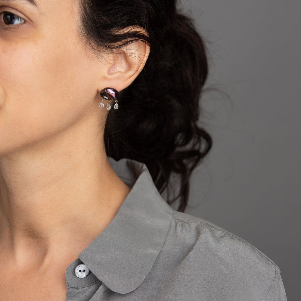 woman in grey modeling dark peacock keshi pearl earring in cloud-like form with three white topaz dangling from the bottom with yellow gold components