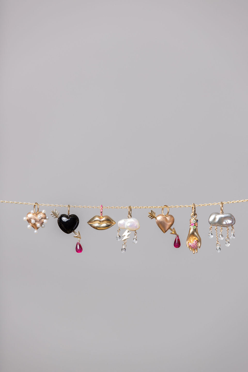 multiple different rachel quinn jewelry charms dangling from a gold chain horizontal with grey background