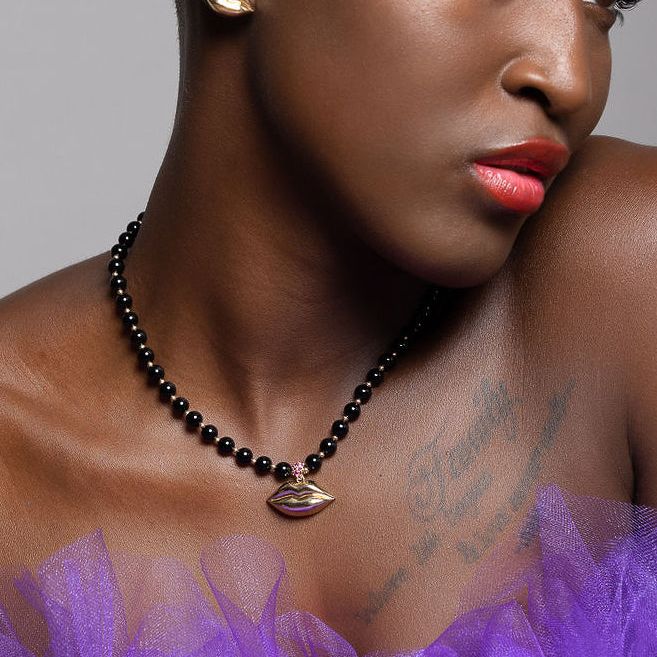black model wearing gold lip earrings and black and gold lip necklace and purple dress