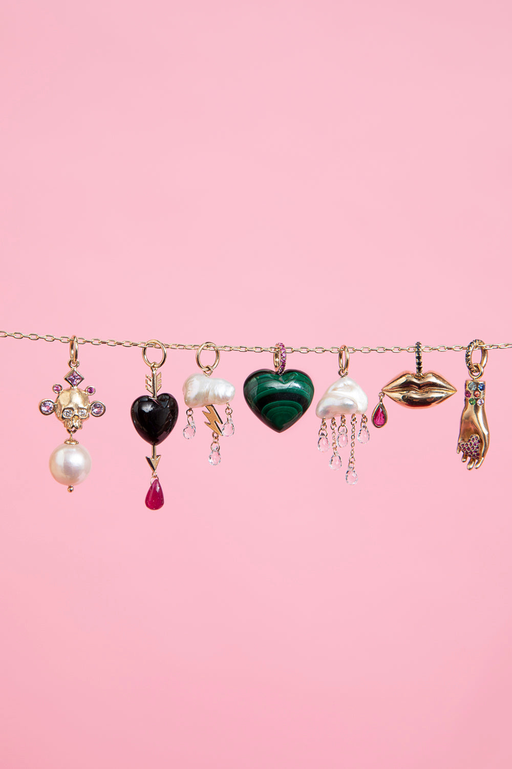 7 Rachel Quinn Jewelry Charms hanging horizontally across a chain on a pink background.