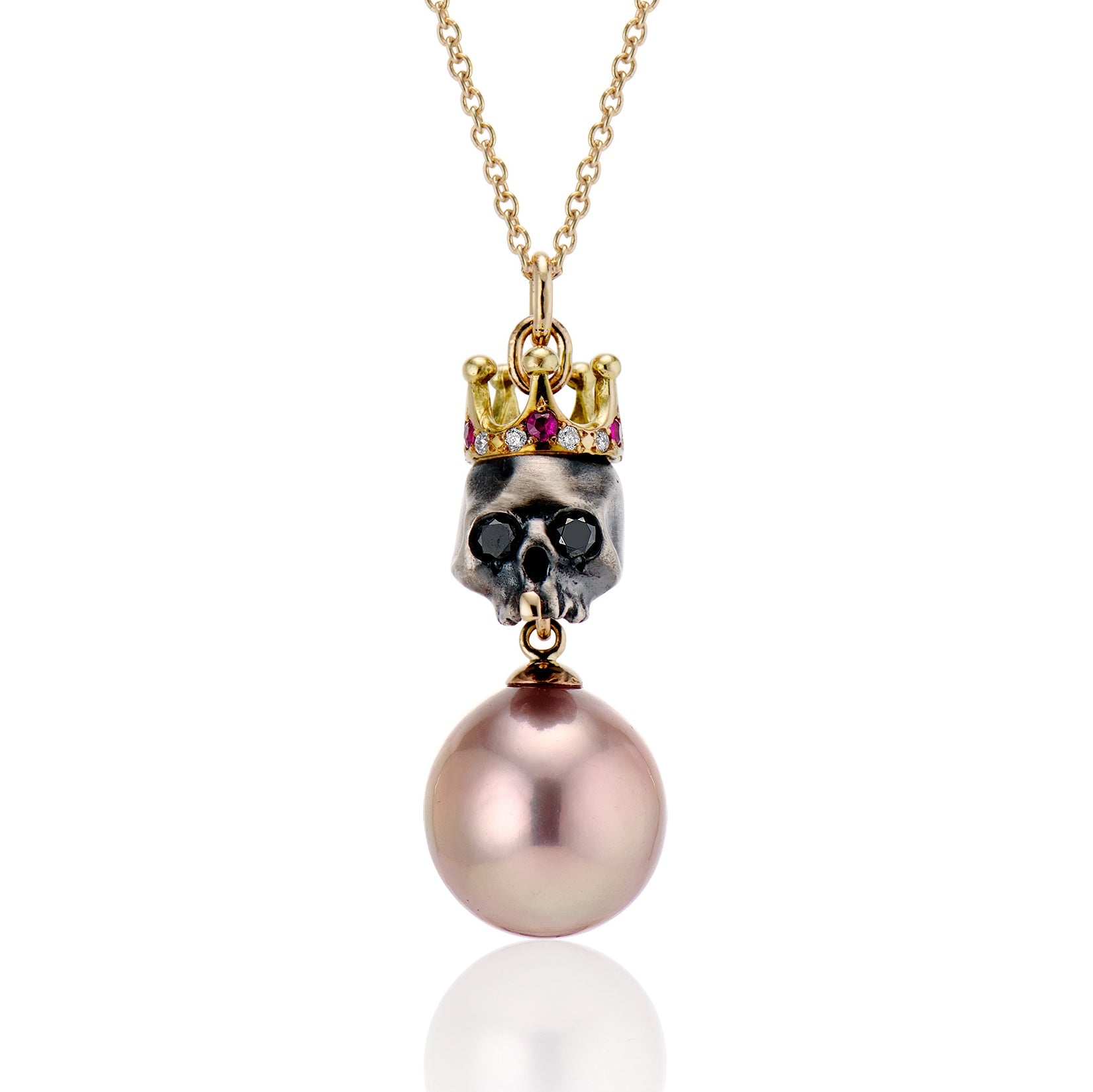 Close up of silver skull with black domain eyes, a gold front tooth, a gold crown with gemstones, and pink pearl hanging below on a white background.