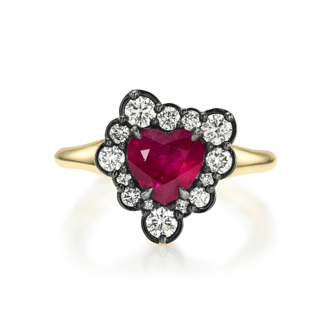 A yellow gold ring featuring a heart-shaped ruby center stone surrounded by a halo of round diamonds against black rhodium, set against a clean white background.