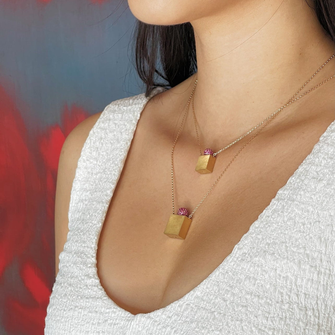 Close-up of a person in white wearing two gold memorial box necklaces for ashes with a blurred background
