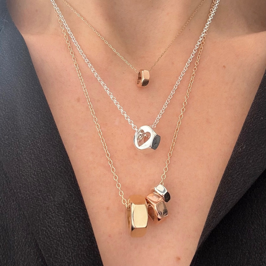 Three hex nut necklaces in yellow and rose gold and silver on a person wearing a black top.