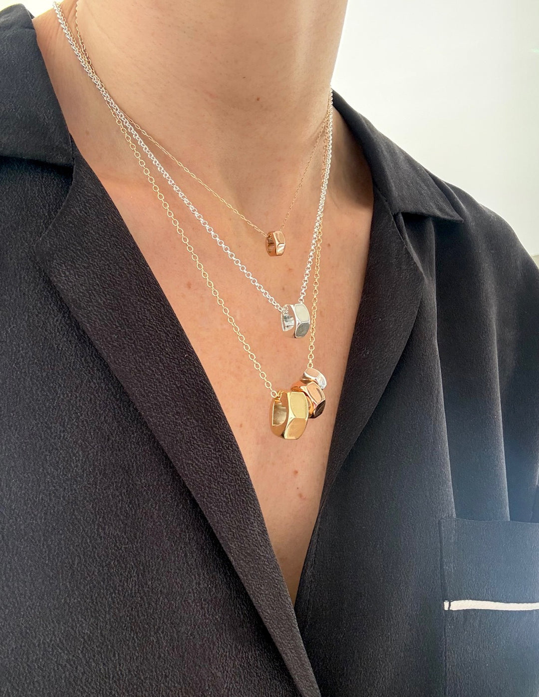 Close-up of a person wearing a black shirt and multiple chain necklaces with hex nut pendants in various sizes and metal colors.