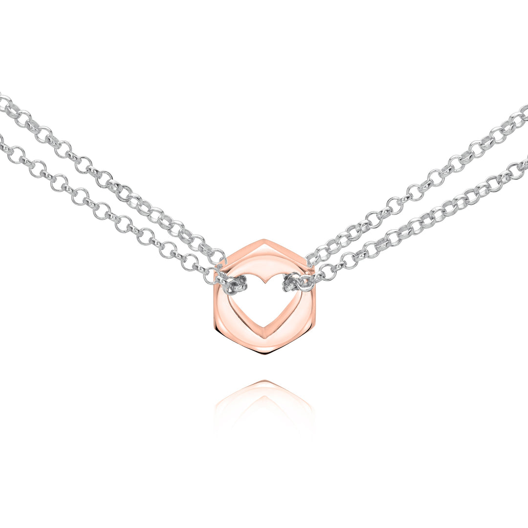 Close up of a rose gold hex nut pendant with silver chains holding it from either side on a white background