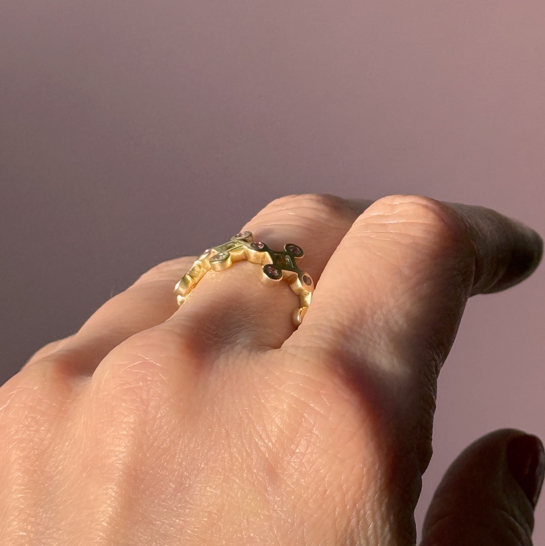 Side view of a yellow gold ring with pink and green gemstones on a neutral background