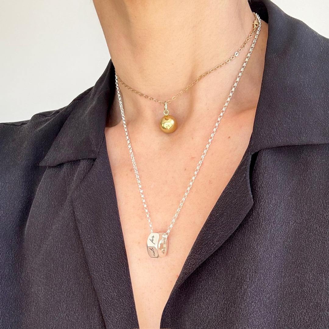 Close up of person in a black shirt wearing a gold ball choker necklace and silver hex nut on silver chain necklace against light grey background. 