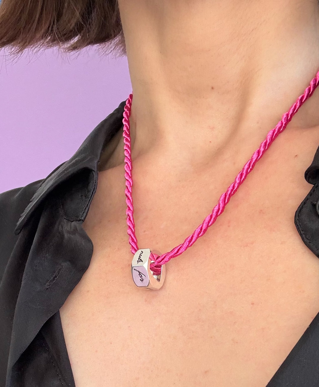 Person in black shirt wearing a pink corn necklace with a hex nut engraved pendant  against a purple background