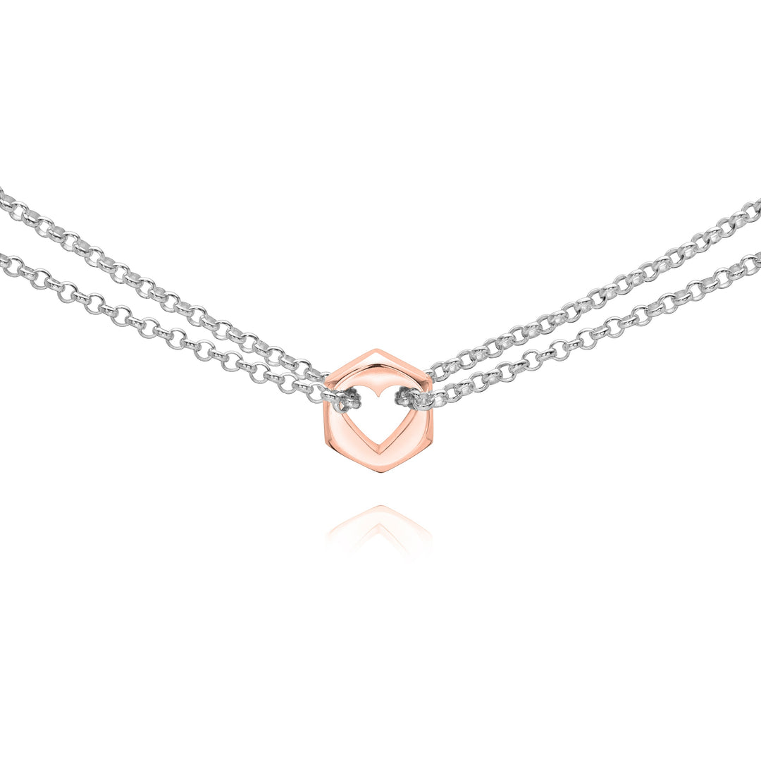 Close up of a rose gold hex nut charm with silver chains holding it from either side on a white background