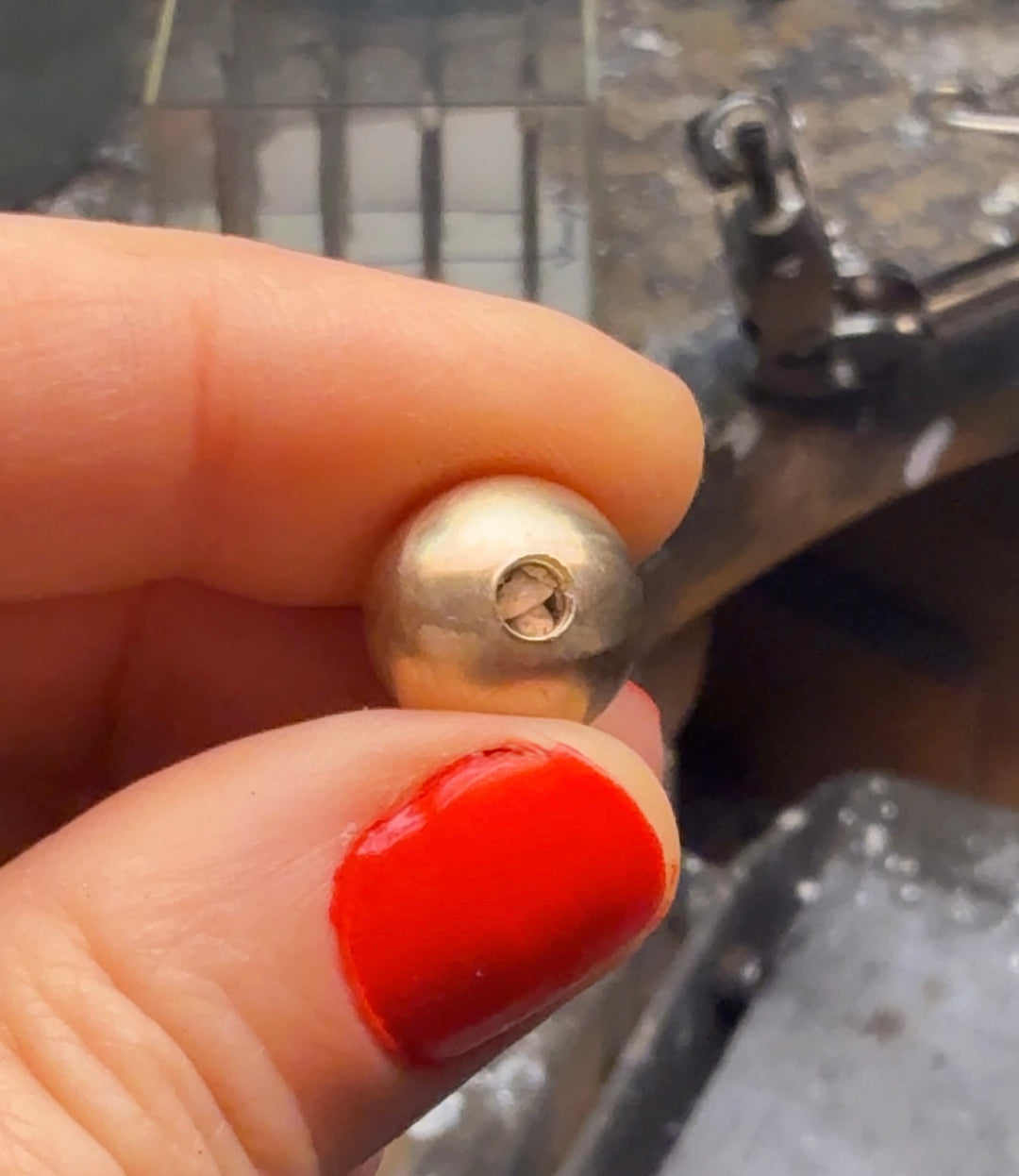 Gold-colored knob held by a hand with red nail polish, with a blurred background