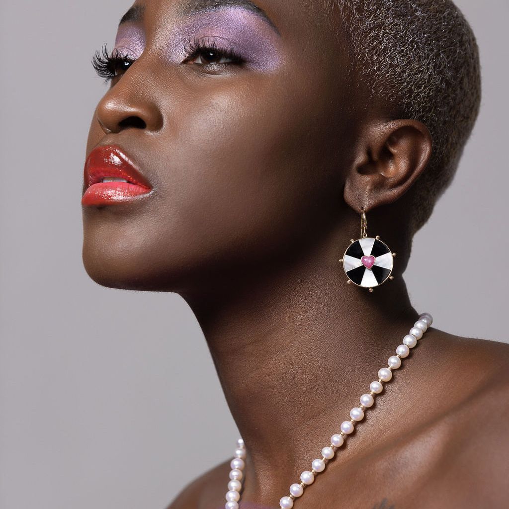 black model on a grey background with shaved head wearing purple and both bullseye heart necklace and earrings