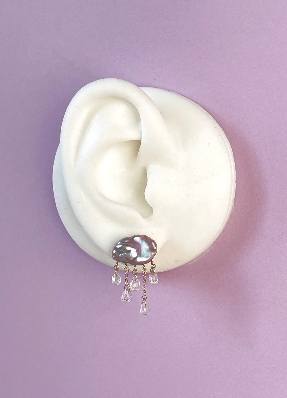 white ear shape one purple background with grey cloud-shaped pearl earring with 5 raindrops dangling below