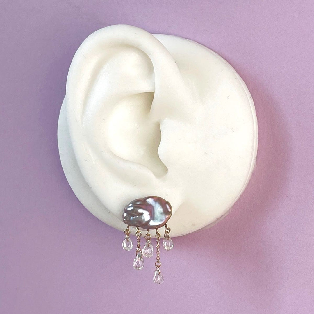 white ear shape one purple background with grey cloud-shaped pearl earring with 5 raindrops dangling below