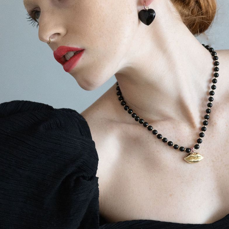 red head model wearing black heart earrings and gold & black lip necklace