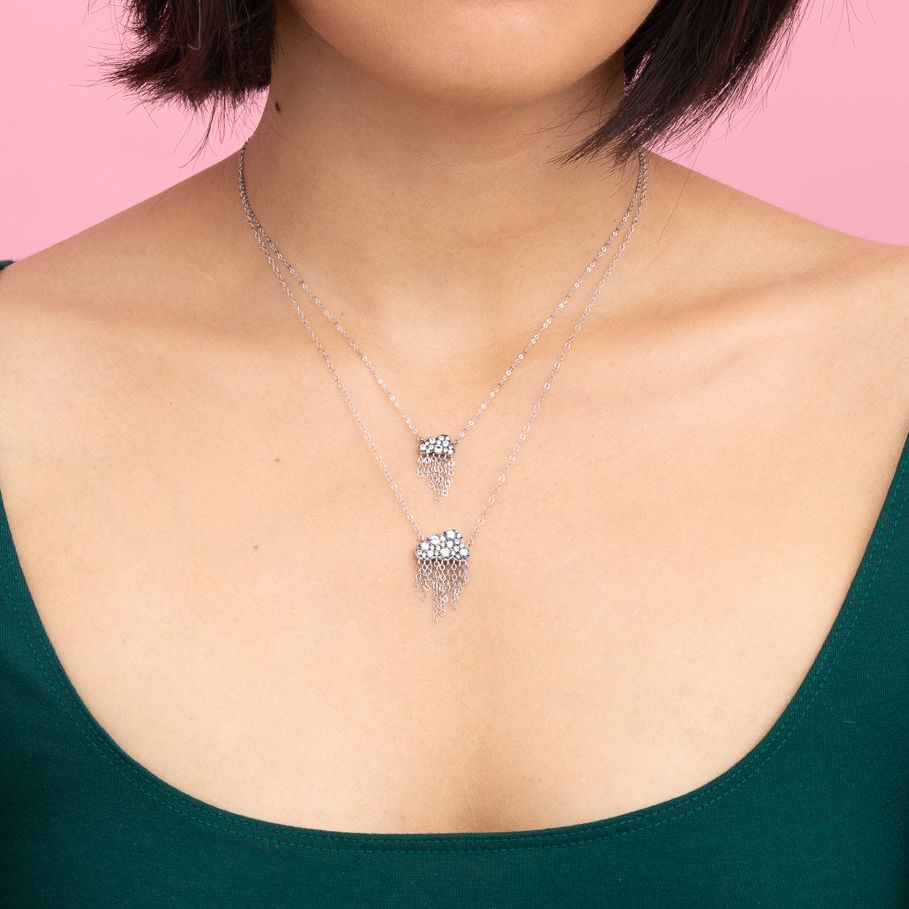 Rachel Quinn Jewelry black cloud shaped necklace in small and large with pave white sapphires on cloud and dangling chains worn on female model neck.