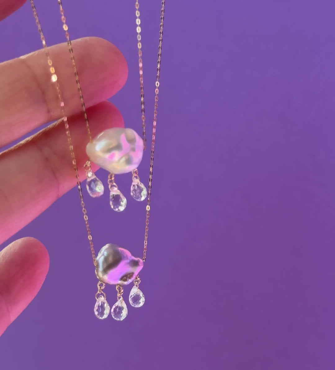 Video of two pearl cloud pendants with clear gemstone raindrops dangling from below against a purple background