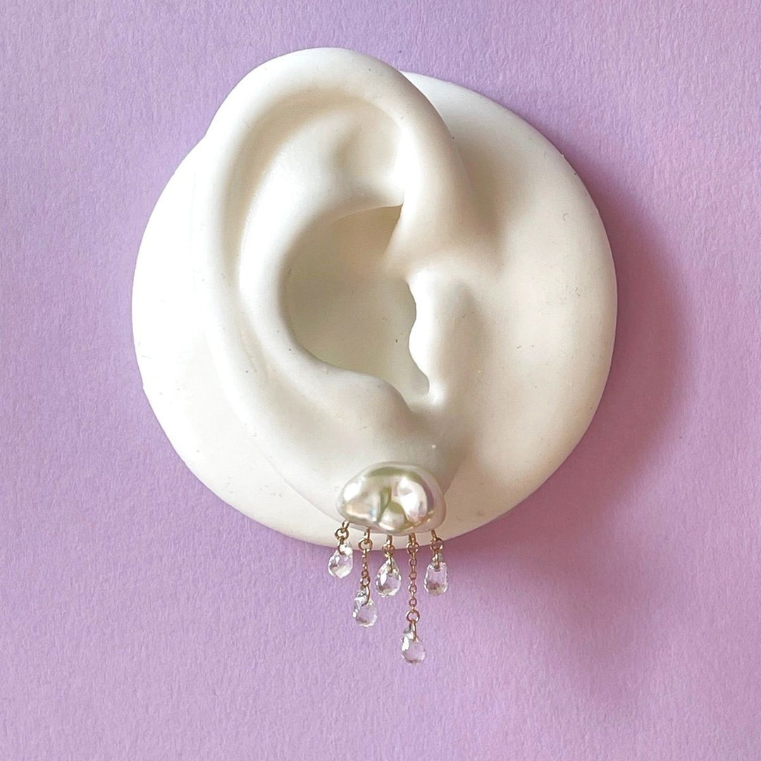 white ear shape one purple background with white cloud-shaped pearl earring with 5 raindrops dangling below