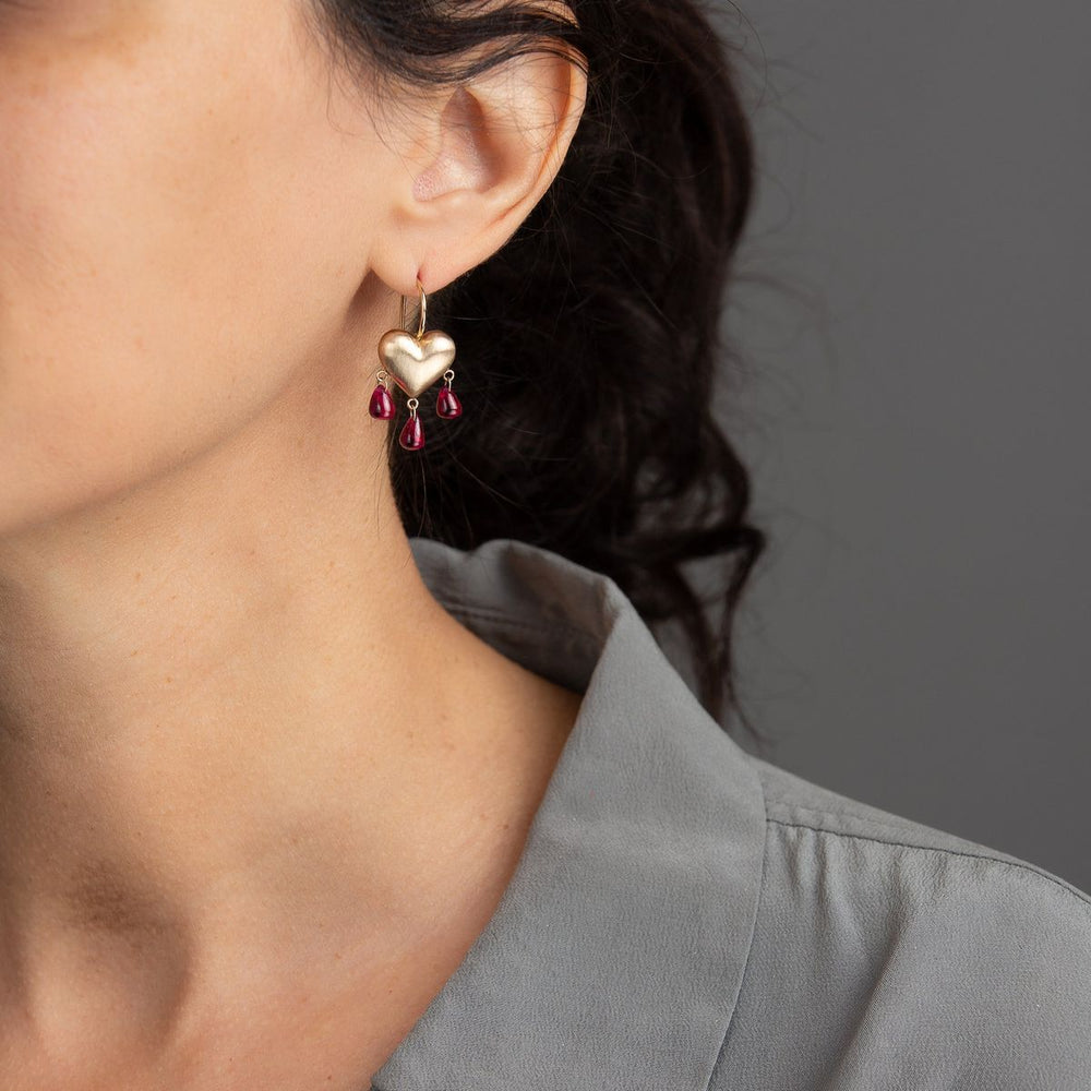 Woman in grey blouse wearing gold heart earrings with pink ruby drops