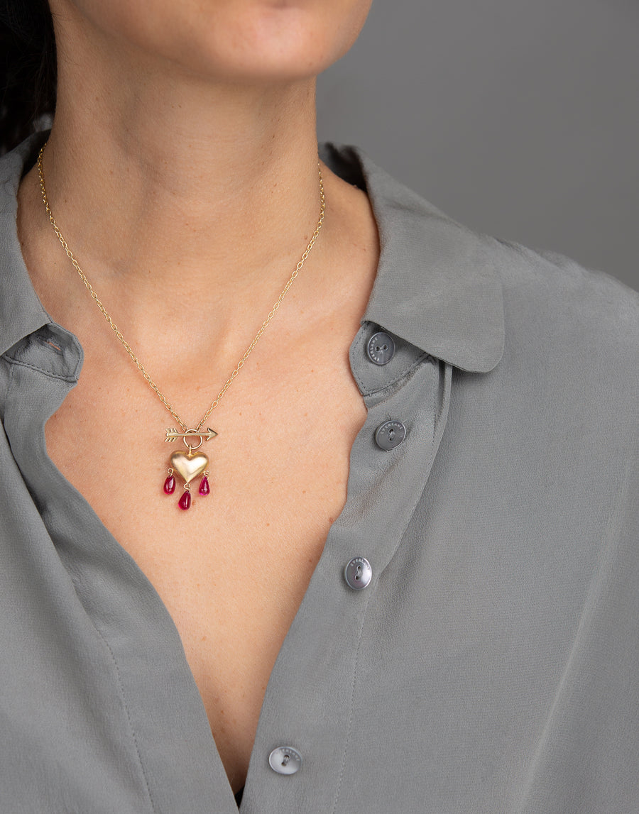 Woman in grey blouse wearing yellow gold puffed heart necklace with pink ruby droplets