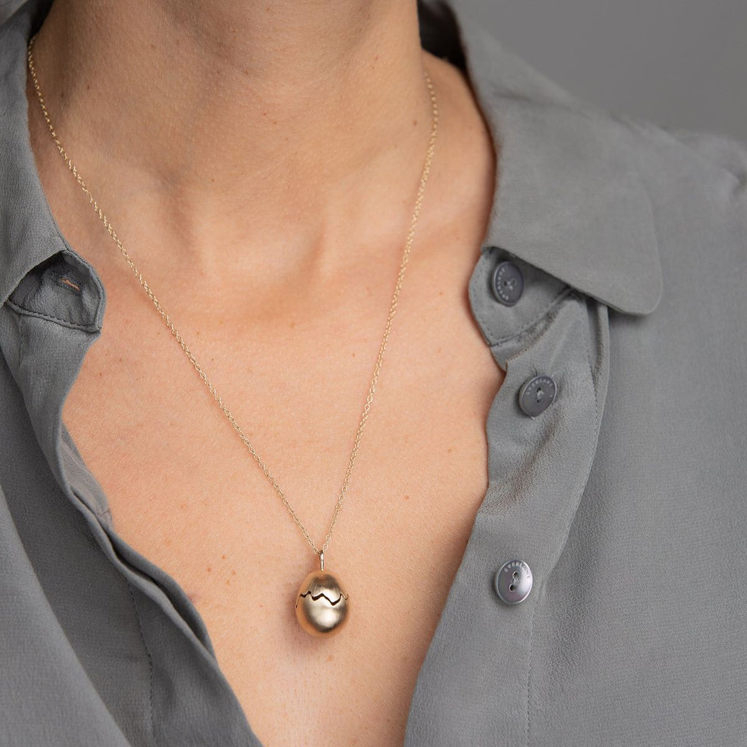 Woman in grey blouse wearing yellow gold broken egg necklace.