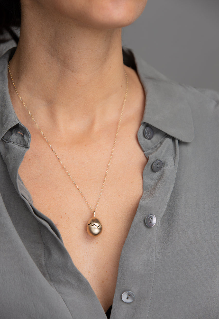 Woman in grey blouse wearing yellow gold broken egg necklace.
