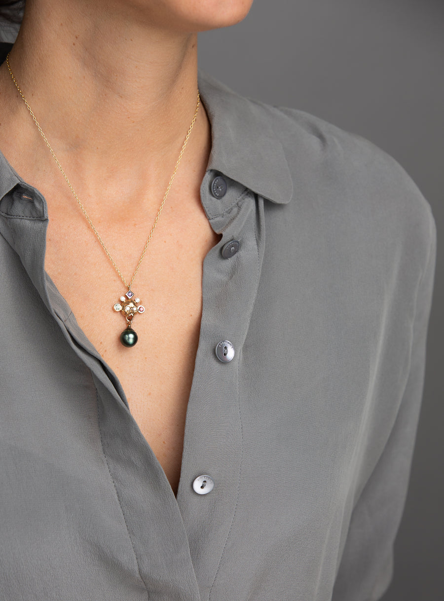 Woman in grey blouse wearing yellow gold skull pendant with gemstones and green pearl