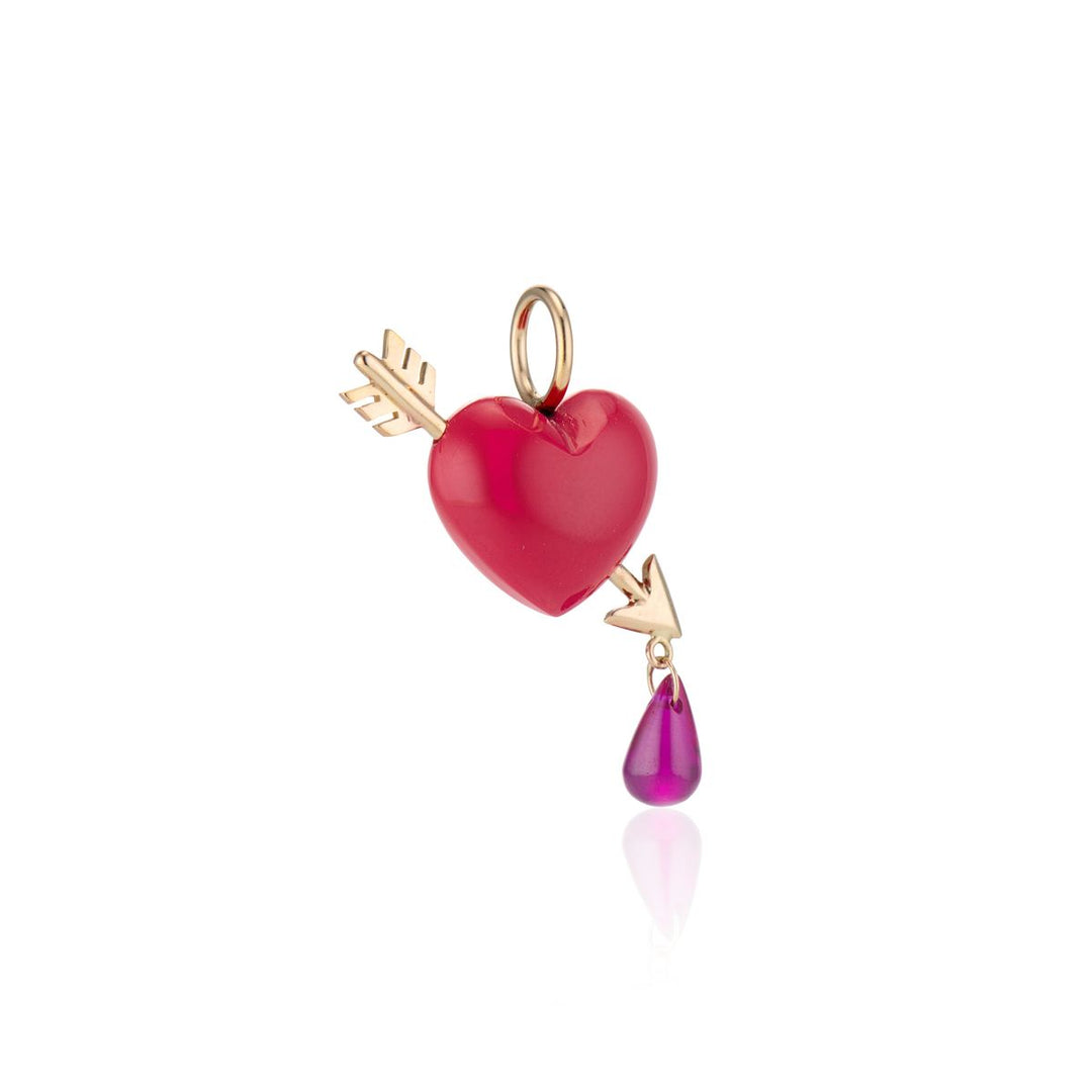 angled view of coral heart with gold arrow pierced through it at an angle with one red rby droplet hanging off point of arrow with gold bail