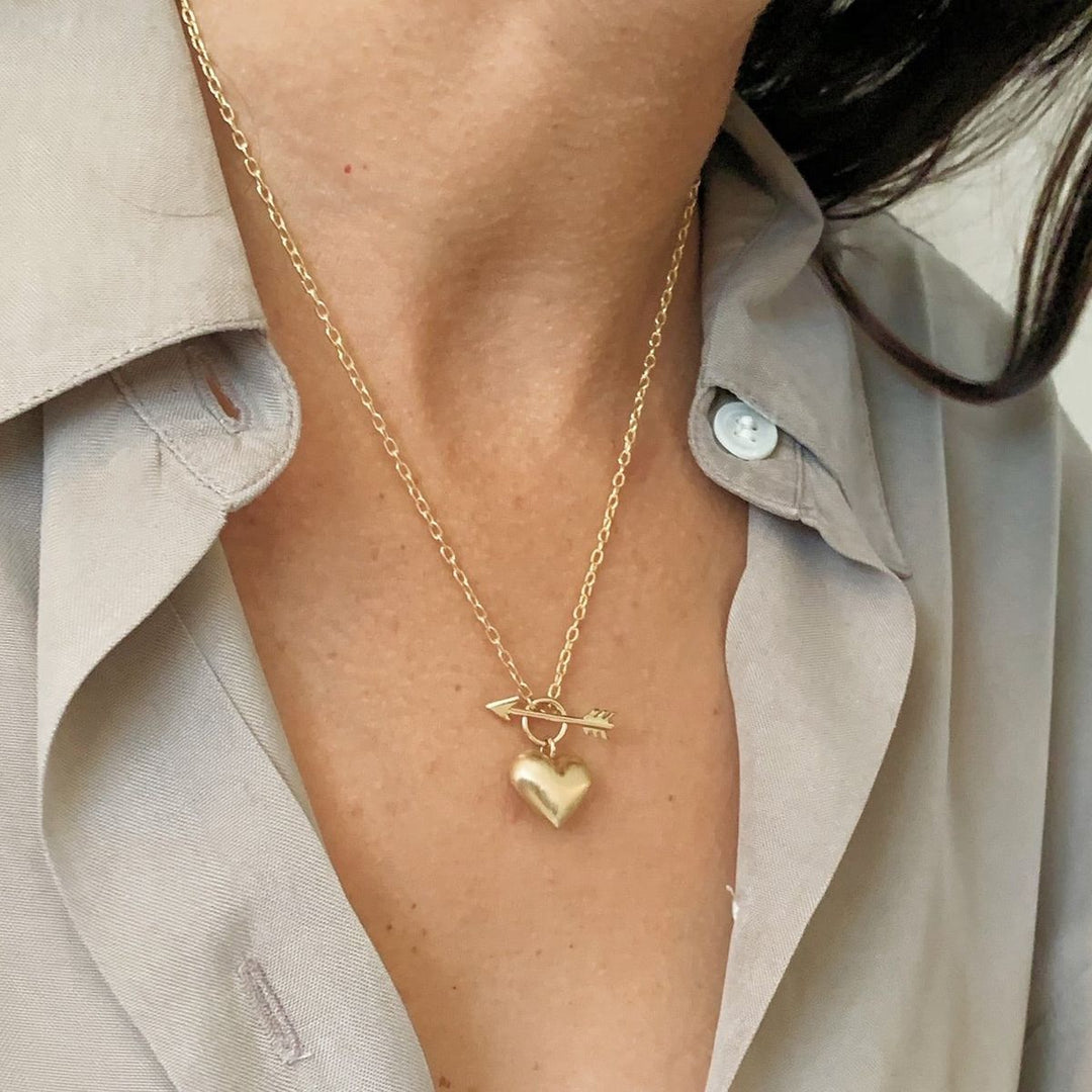Woman wearing a small yellow gold puffed heart pendant on a chain link necklace with a front arrow toggle clasp