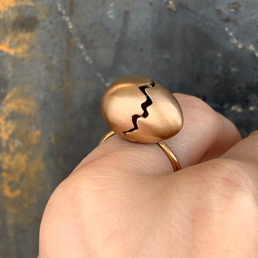 Yellow gold broken egg ring on finger in front of grey wall