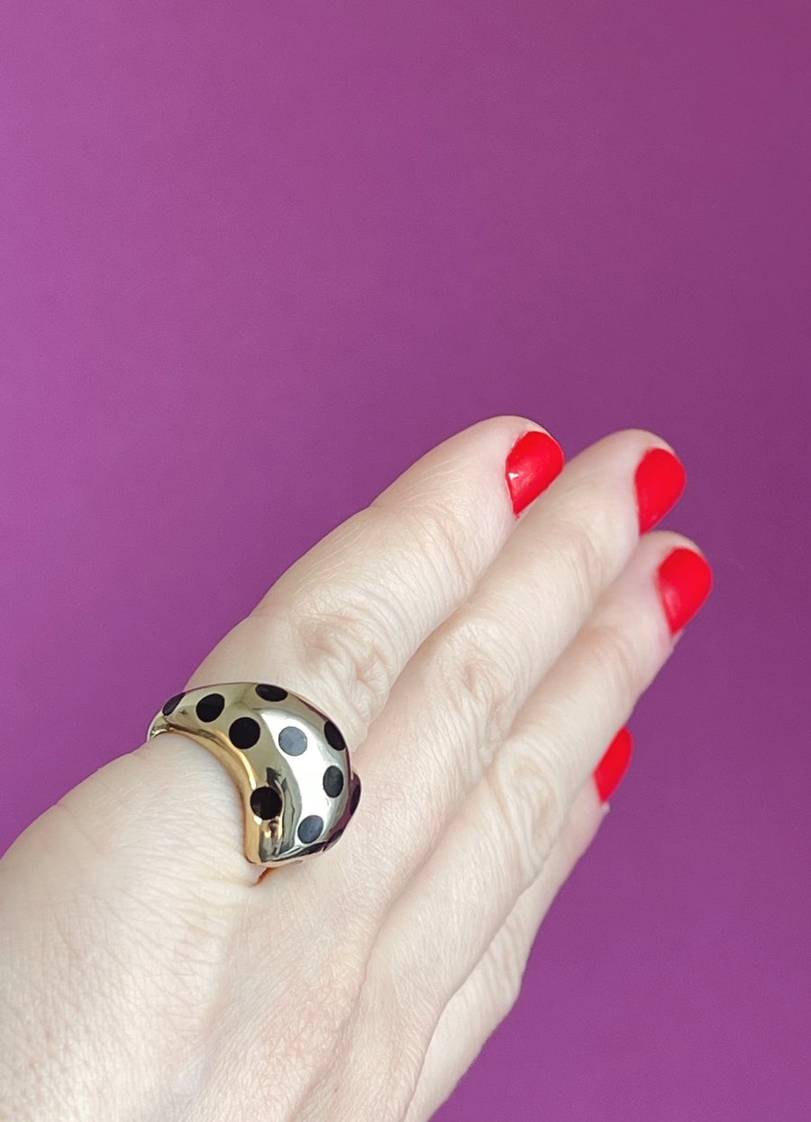 angled view of gold chubby heart ring with black polka dots on a pinky finger to show how the ring wears