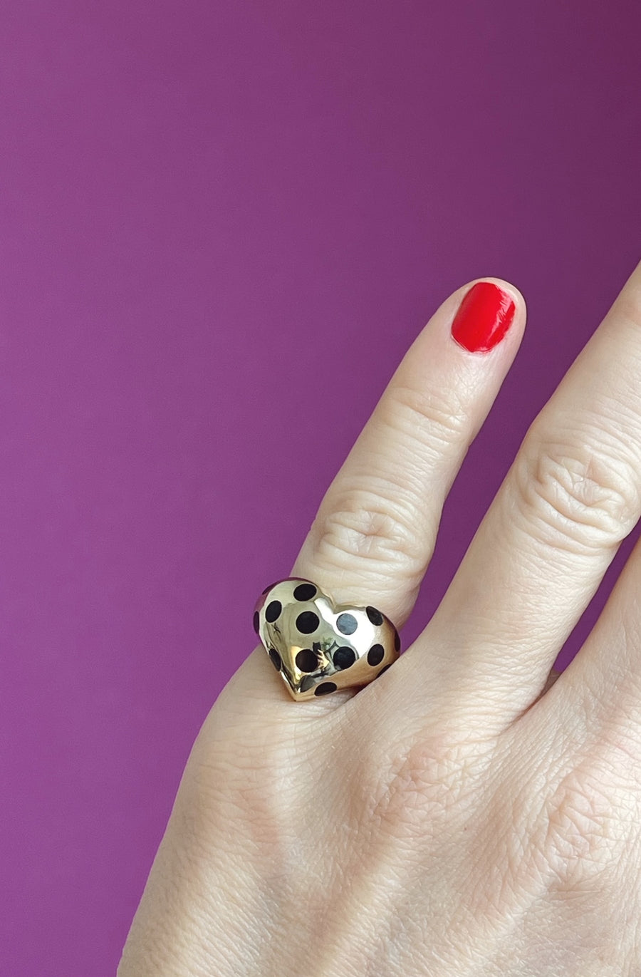 gold chubby heart ring with black polka dots on a pinky finger on a pink background